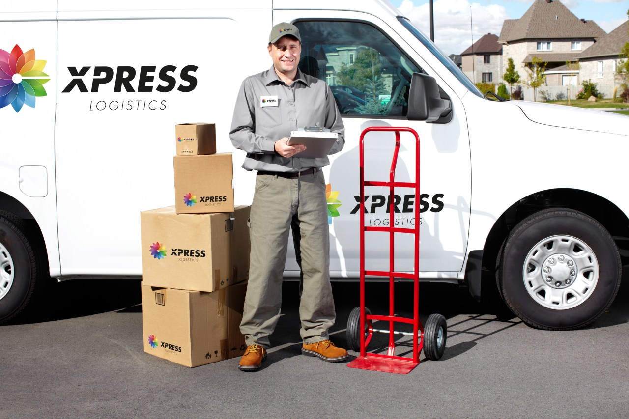 Express delivery man standing in front of a van and next to a stack of corrugated boxes with a colorful logo printed on the box.