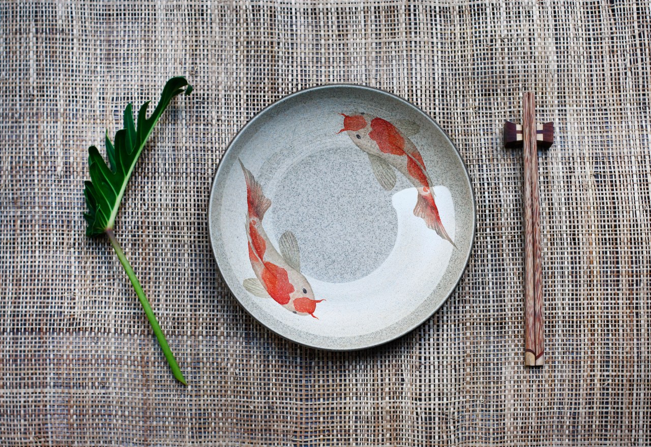 Ceramic dish decorate with coy fish and chopsticks on a bamboo mat.
