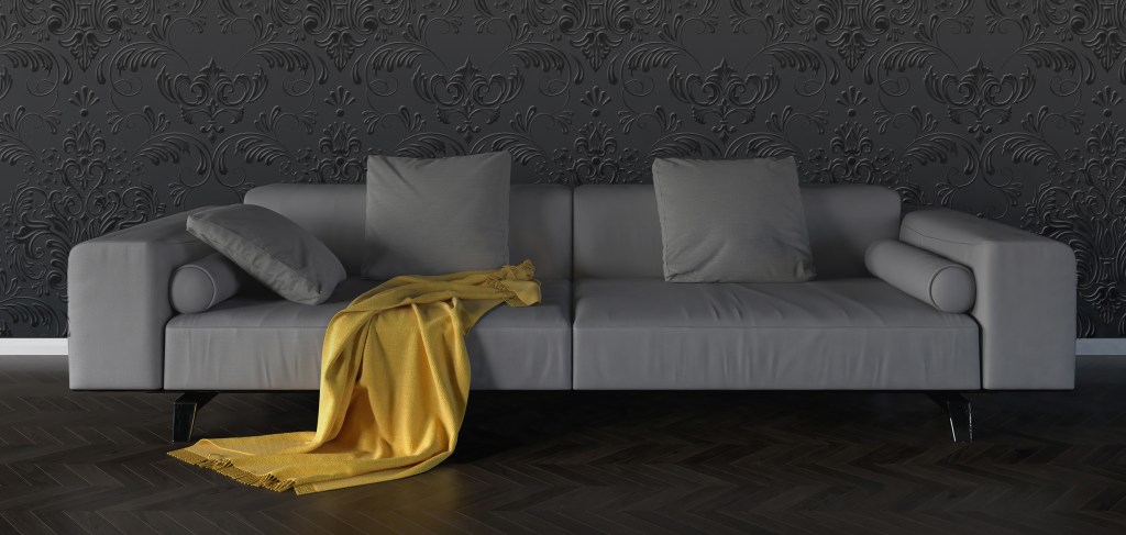 Couch with a yellow throw blanket in front of a wa with gray textured wallpaper.